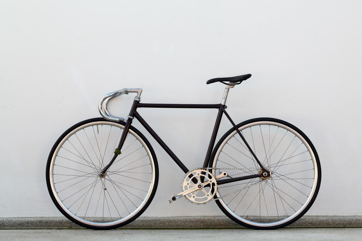 Minimalist single-speed bicycle with chrome handlebars leaning against a white wall on a concrete ledge